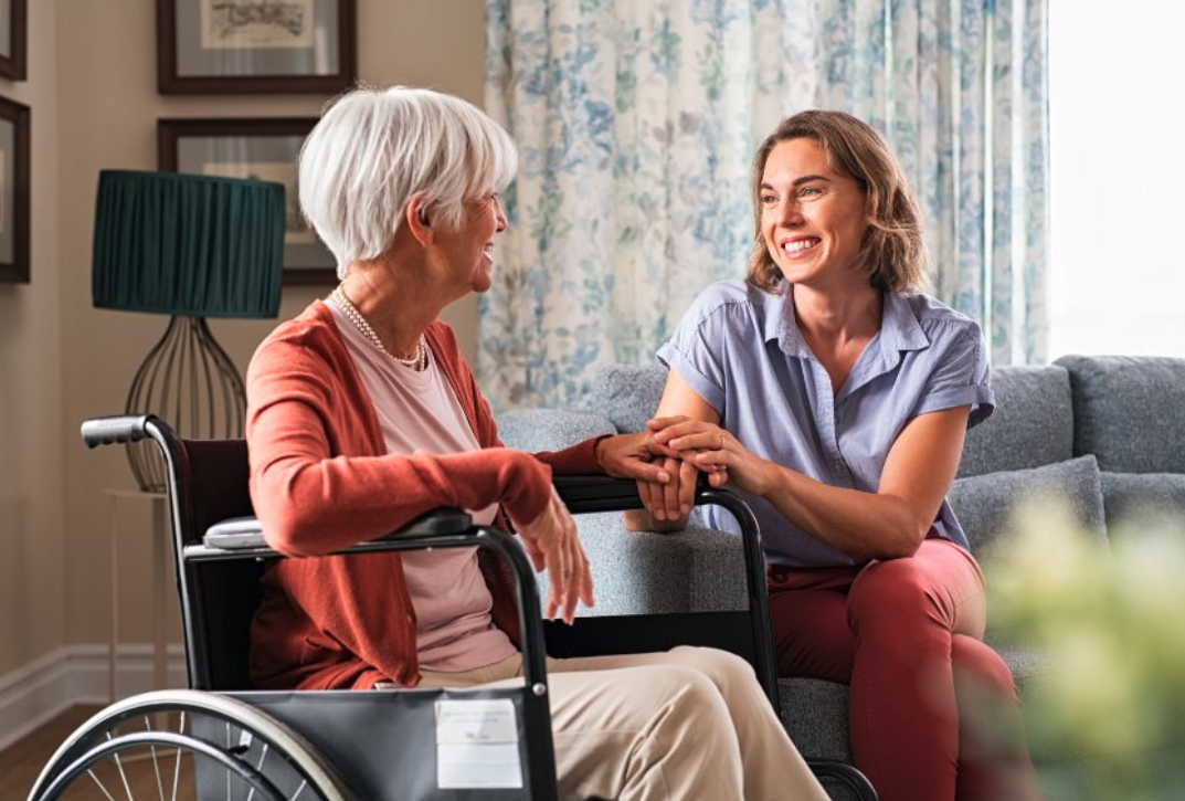 Caregiver holding hands with elderly woman in wheelchair, sharing a warm moment together